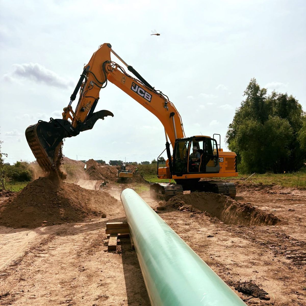 JCB excavator working beside strung pipe on the right-of-way