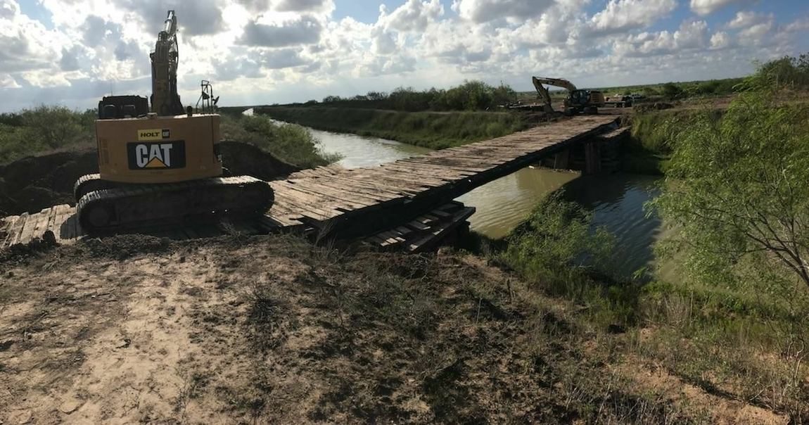 Excavator crossing a temporary timber bridge over a canal